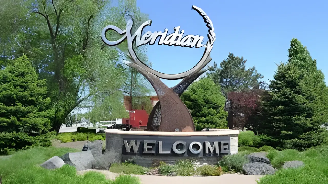 Photograph of the Meridian, Idaho city entry sign with its sculptural arch — landscaped trees framing the WELCOME marker, the city served by Boise Bug Bombers